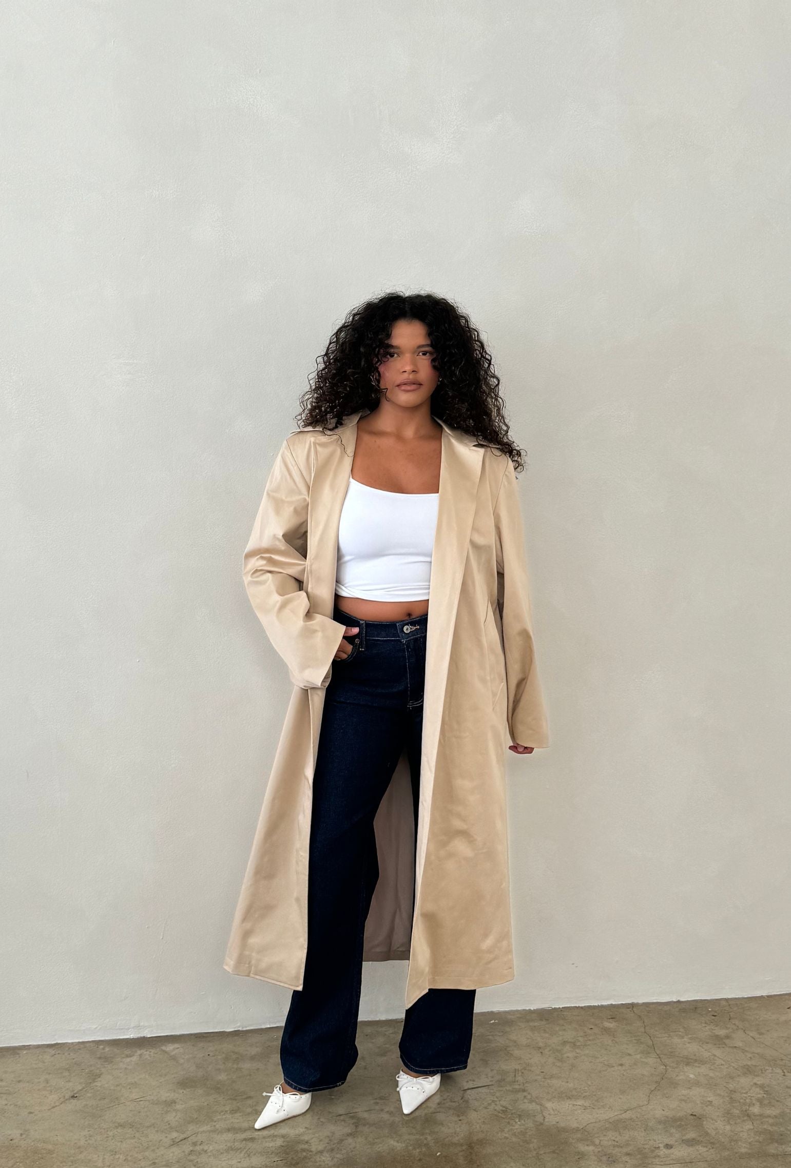 Beige trench coat layered over a white cropped tank and dark denim