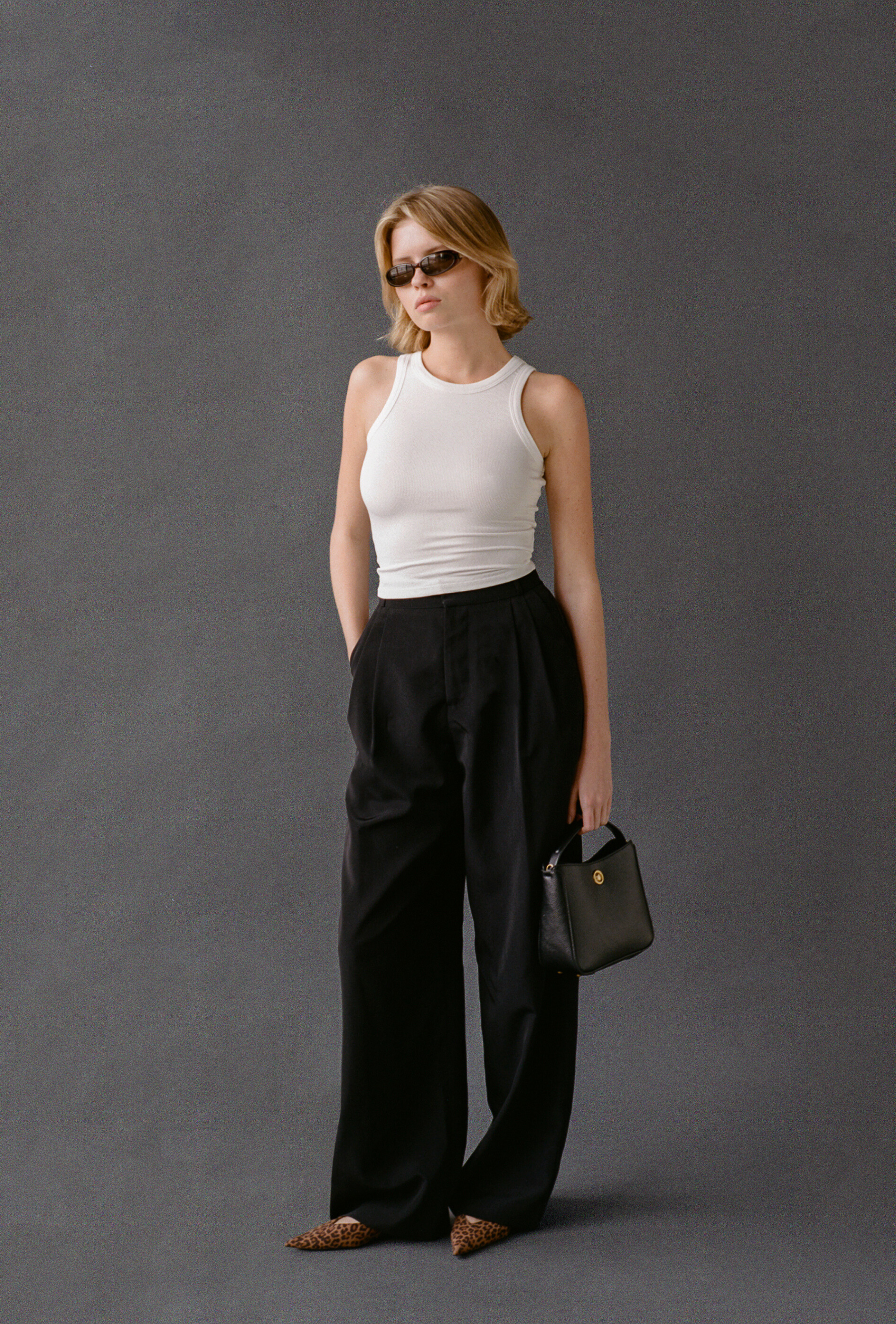 Woman wearing a white tank top and black pants against a gray background