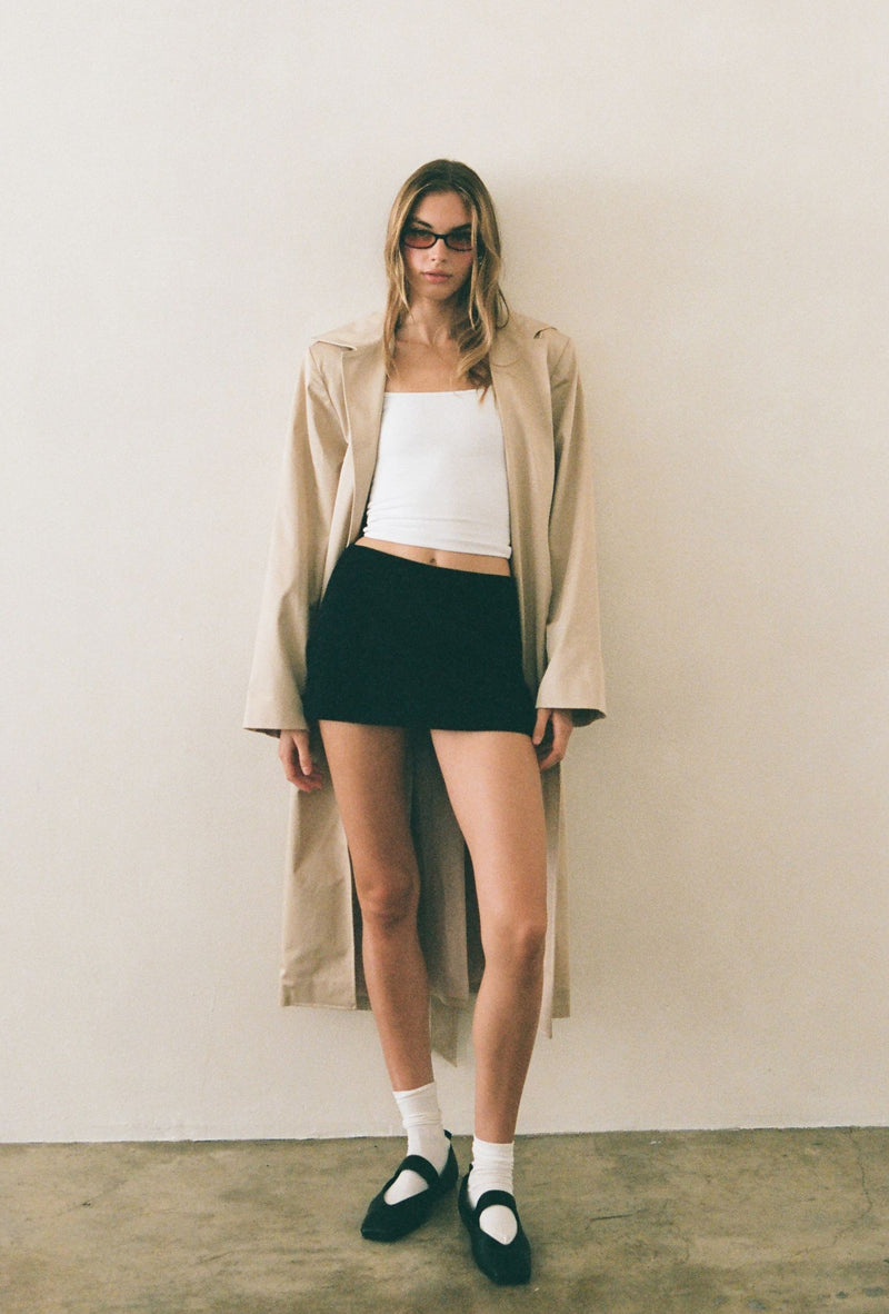 Beige trench coat styled over a white cropped tank and black mini skirt
