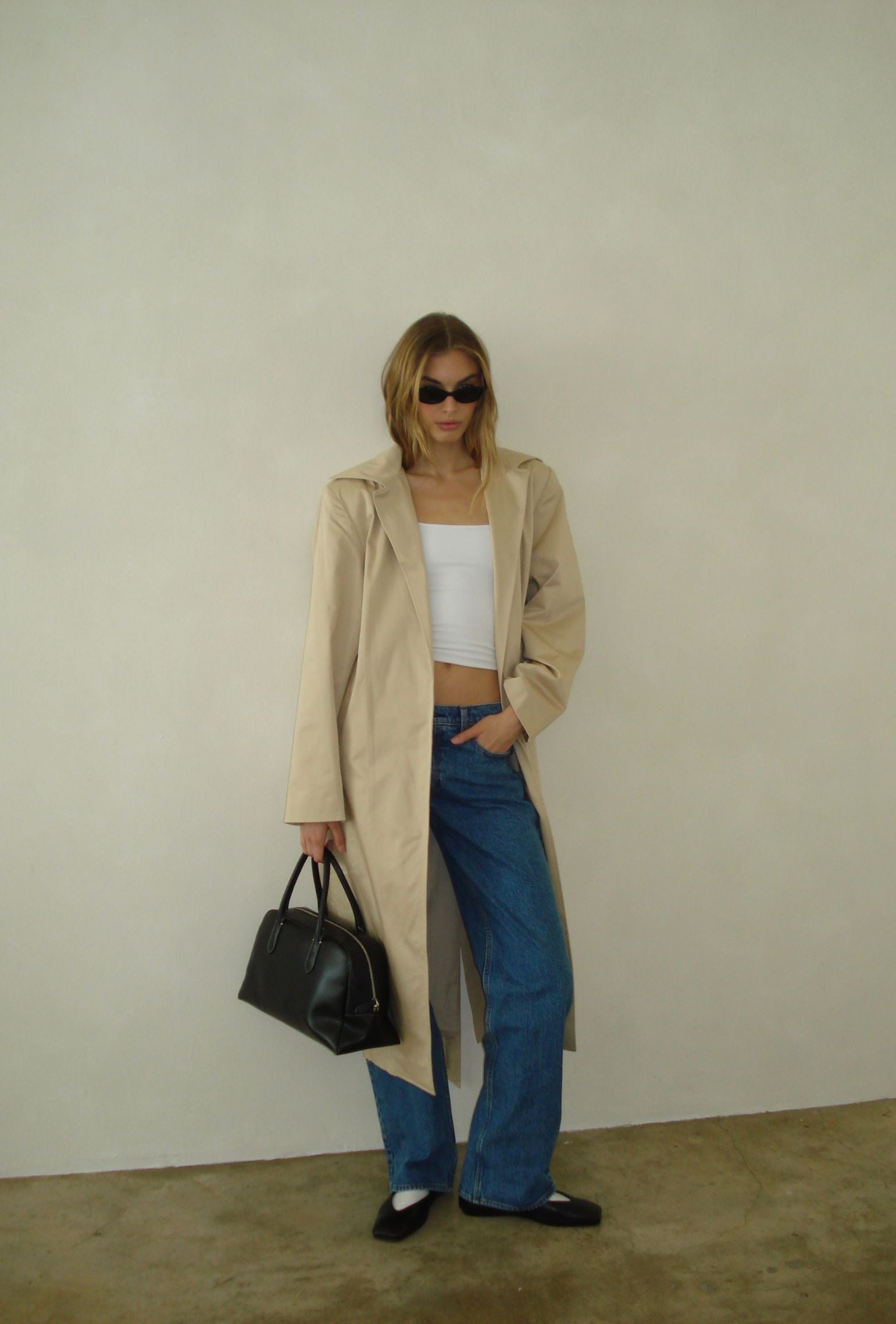 Beige trench coat styled with a white cropped tank and straight leg denim
