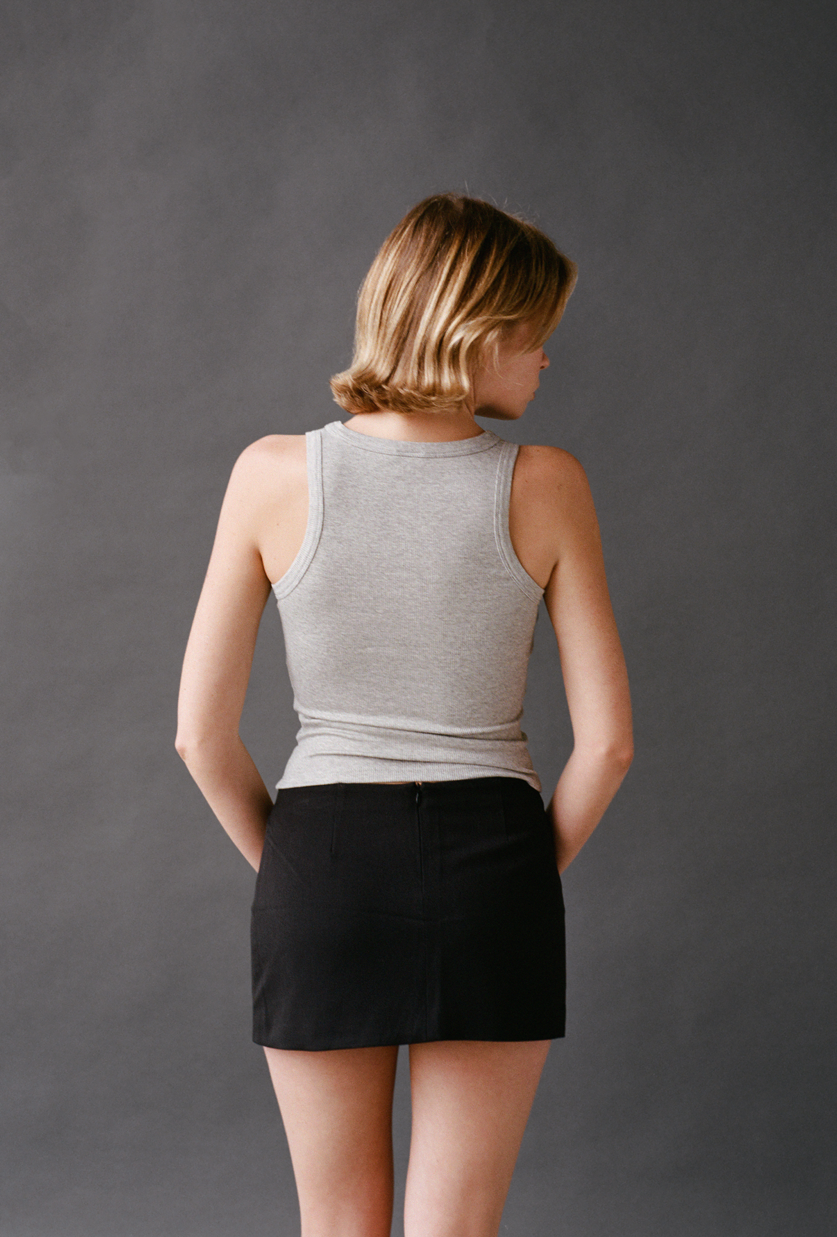Woman wearing a gray tank top and black skirt against a gray background